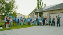 A community group holding blue flags in front of a residential home during the Bighorn Roofing 'Check Your Roof' music video campaign in Utah.